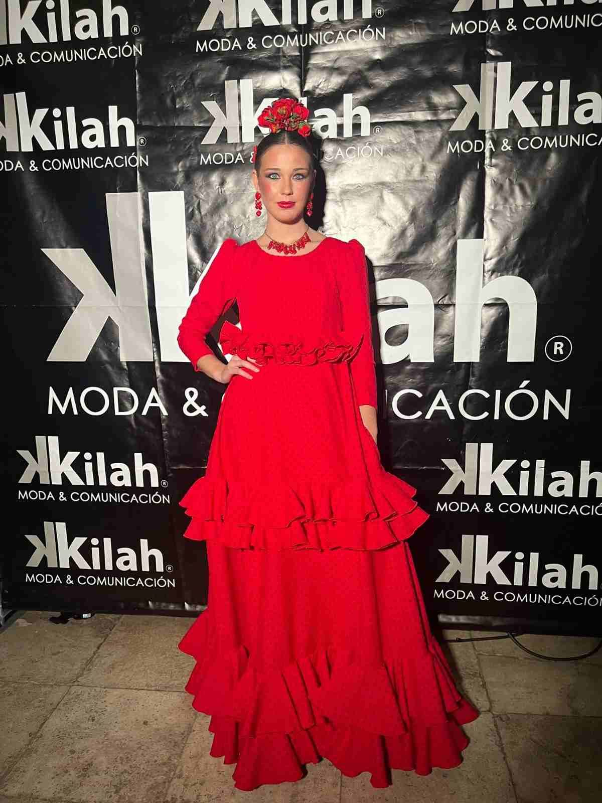 Mujer con un vestido rojo con volantes posando frente al telón de fondo de un evento de Xilah Moda & Celebración