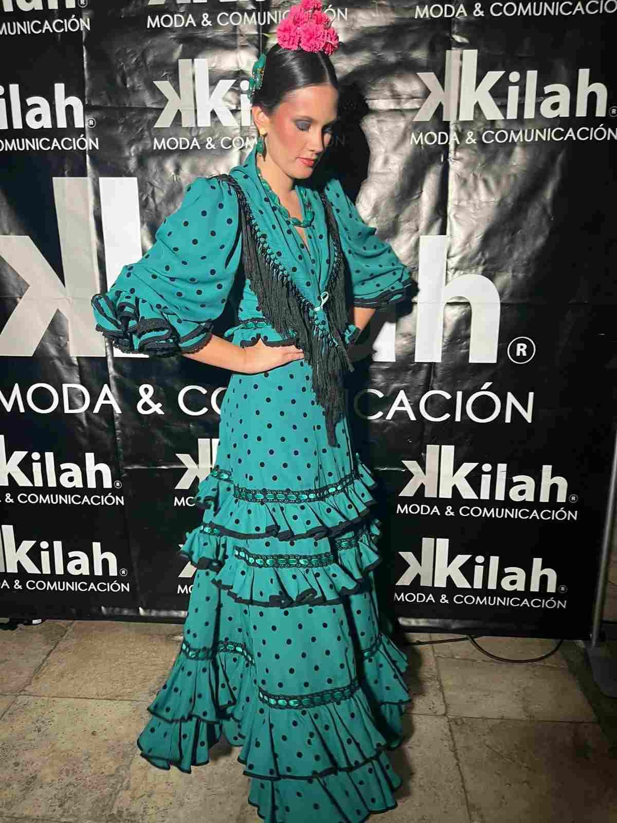Mujer con un vestido turquesa con volantes posando sobre un fondo de photocall para un evento.