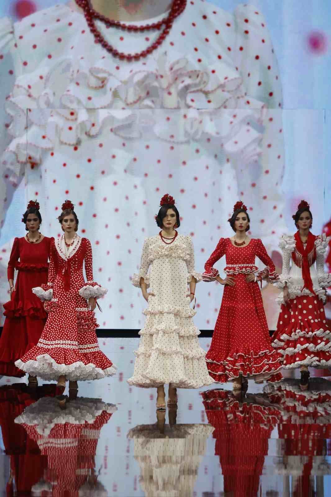 Cinco mujeres con vestidos rojos y crema realizan una danza sincronizada en un escenario.