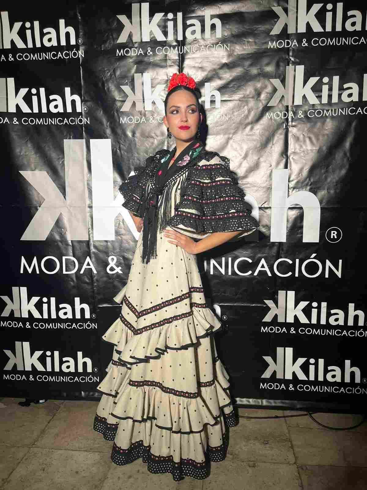 Mujer posando con un vestido negro y crema con volantes frente a un fondo de Kilah Moda & Comunicación.
