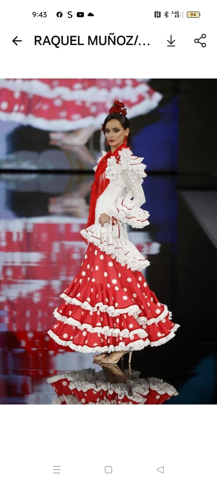 Mujer con un vestido flamenco rojo y blanco con volantes en una pasarela, posando con las manos en las caderas.