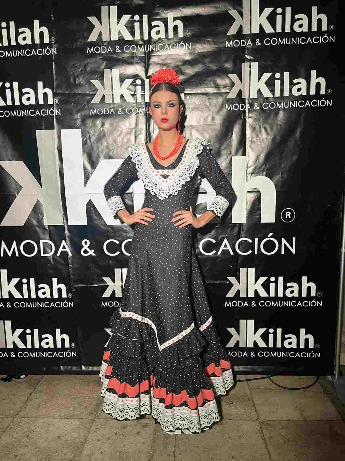 Mujer posando con un vestido bordado en blanco y negro con detalles rojos en el escenario de moda Kilah.