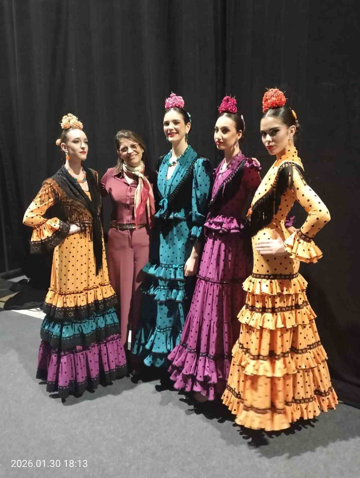 Cinco bailarinas con coloridos trajes tradicionales de flamenco posan frente a un fondo negro.