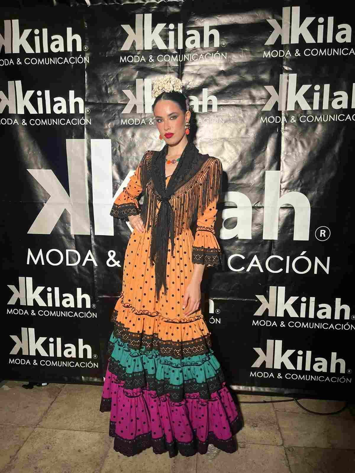 Mujer posando con un vestido naranja y negro en el fondo de un evento de moda de Kilah