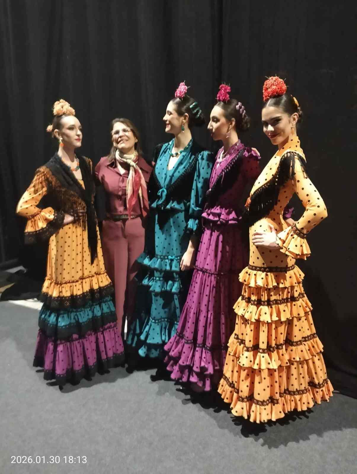 Cinco bailarinas con coloridos vestidos de flamenco posando en el escenario frente a una cortina negra.