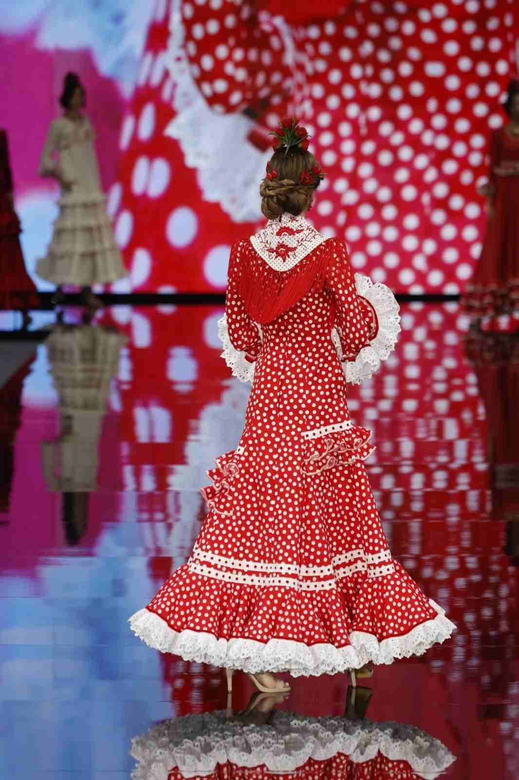 Modelo con un vestido rojo de lunares en una pasarela con un fondo estampado en rojo.
