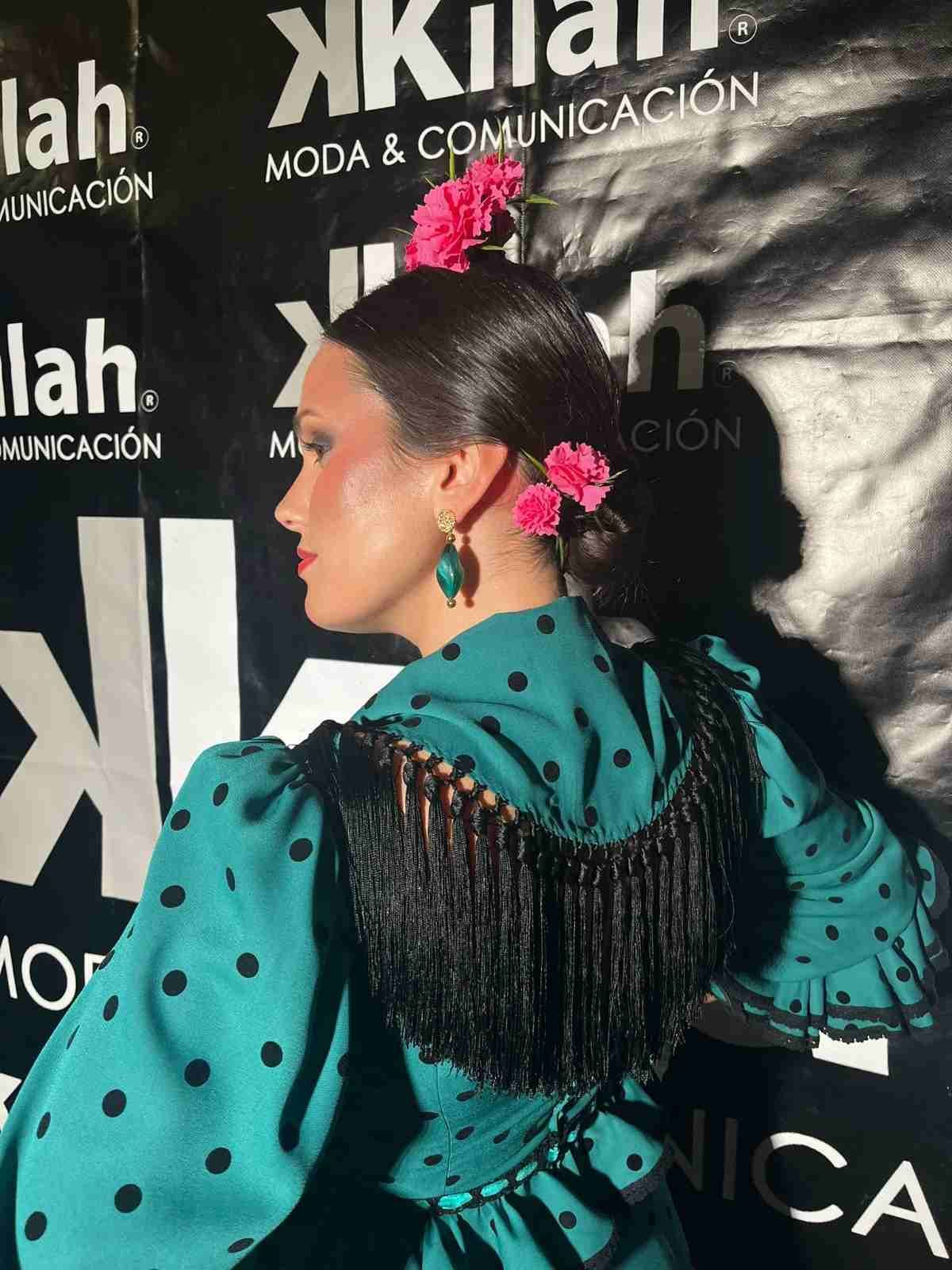 Mujer con vestido flamenco de lunares turquesa posando frente a un evento de moda.