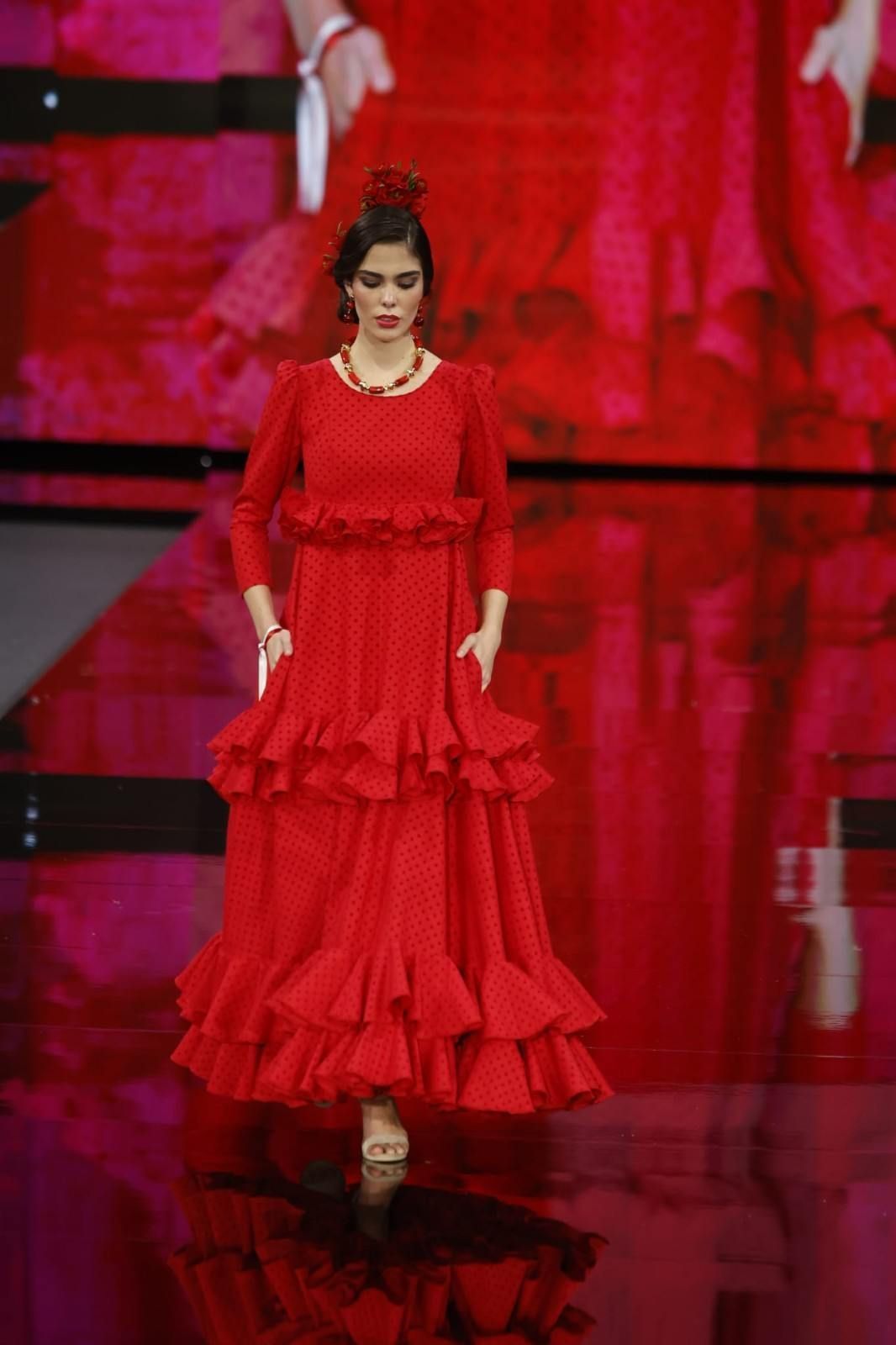 Modelo con un vestido rojo vaporoso desfilando por una pasarela brillante.