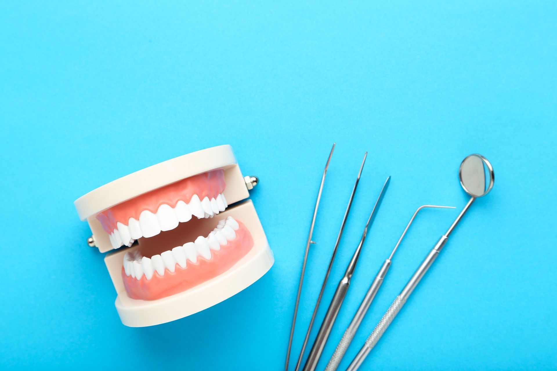 Un modelo de dientes e instrumentos dentales sobre un fondo azul.