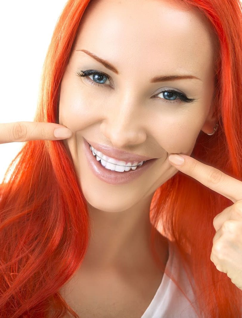 Una mujer pelirroja sonríe y señala sus dientes.