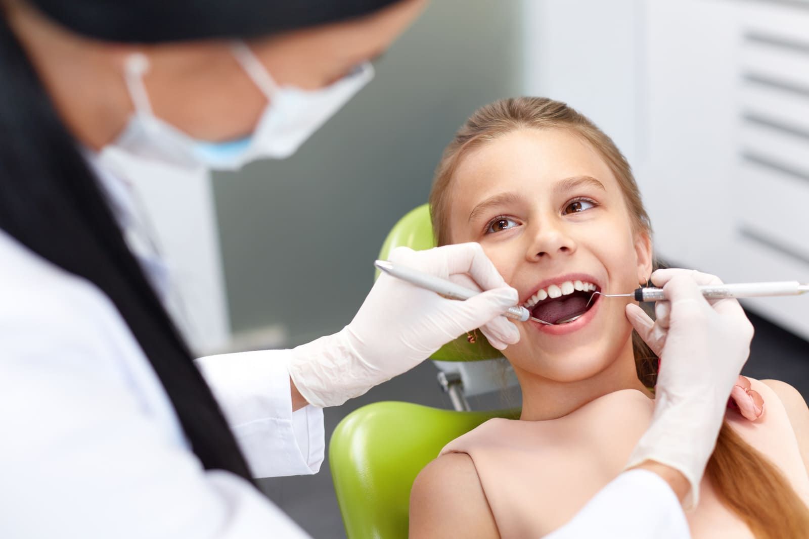 Una niña está sentada en una silla dental mientras un dentista le examina los dientes.