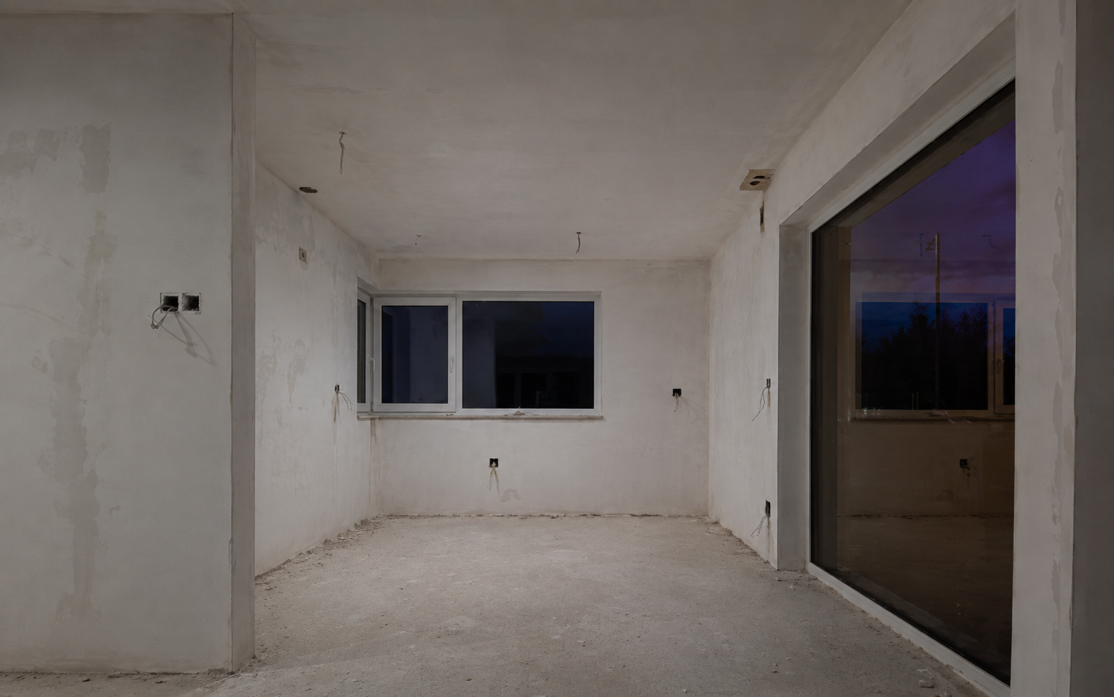 Pièce vide et inachevée aux murs blancs, avec une fenêtre et une porte coulissante en verre au crépuscule