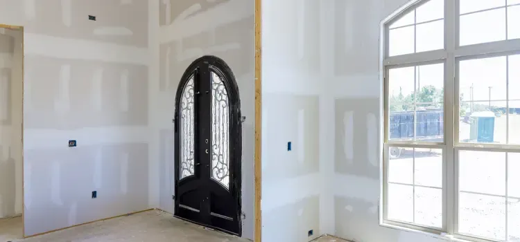 Pièce intérieure aux murs blancs bruts, porte d'entrée cintrée noire et grande fenêtre cintrée.