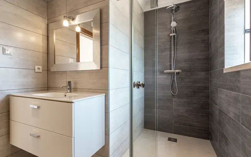Salle de bains moderne avec douche carrelée, meuble-lavabo blanc et miroir.