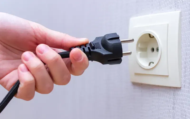 Branchement manuel d'un cordon électrique noir dans une prise murale blanche