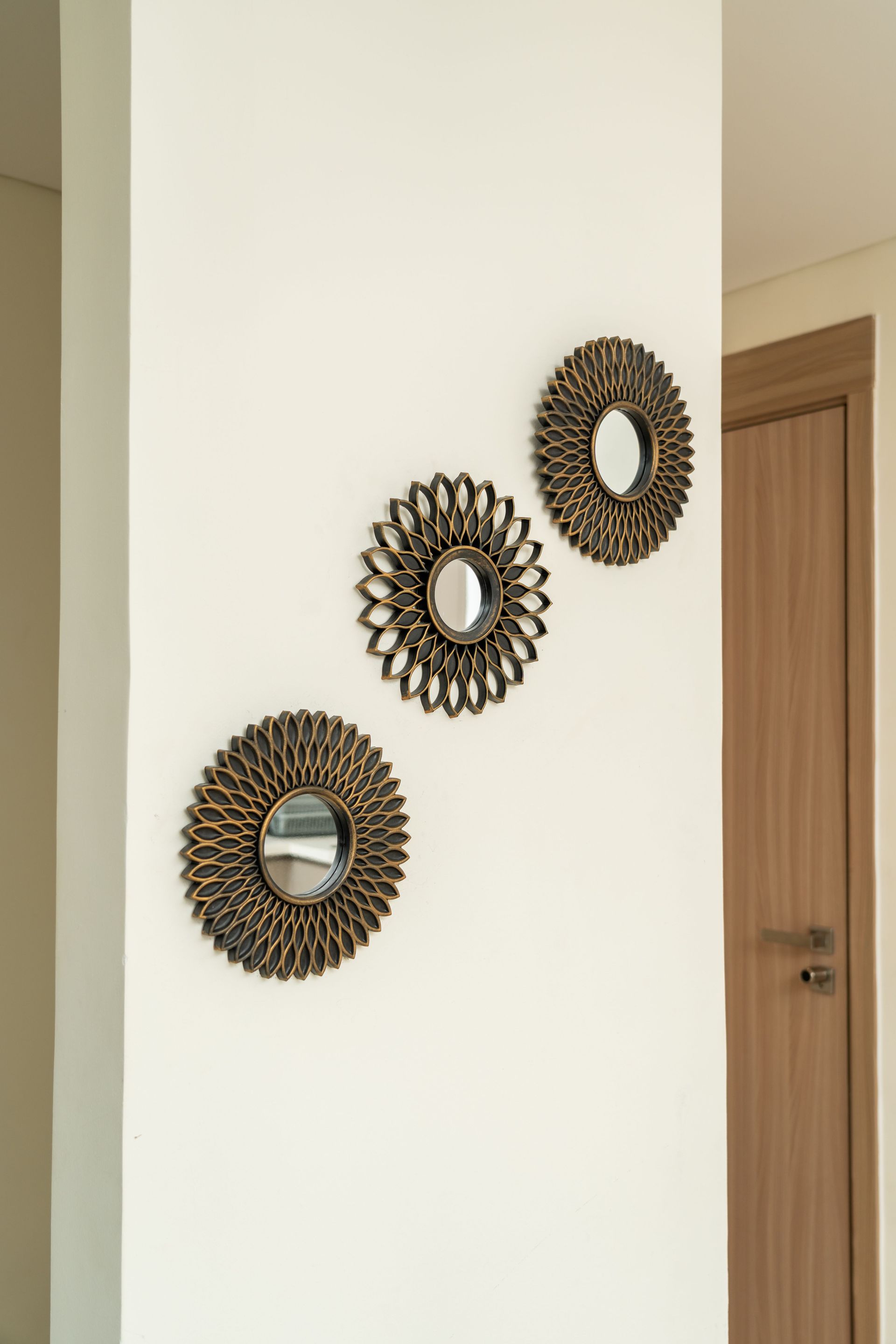 Trois miroirs muraux ronds décoratifs sont fixés sur un mur blanc d'un couloir, à côté d'une porte en bois.