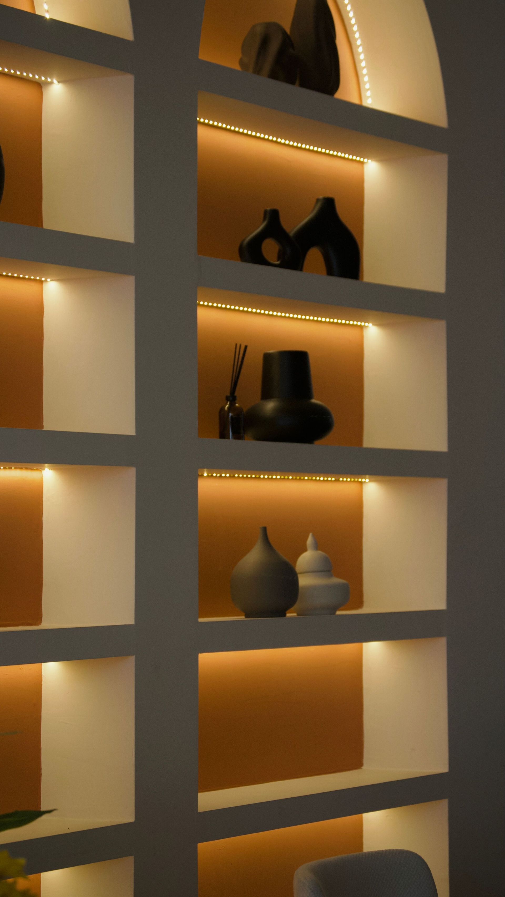 Étagères rétroéclairées avec vases et sculptures décoratives dans une lumière orange chaude