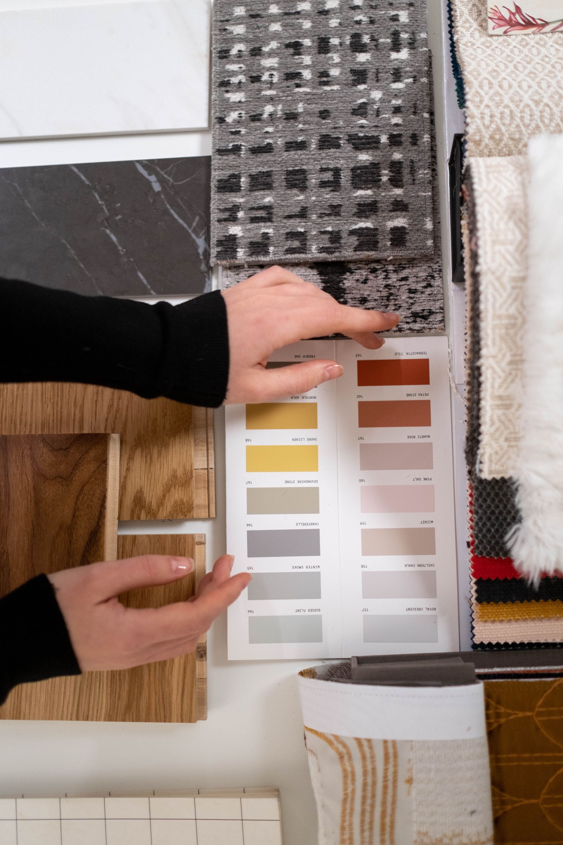 Des mains comparent des échantillons de peinture et de matériaux sur un présentoir d'échantillons de décoration intérieure.