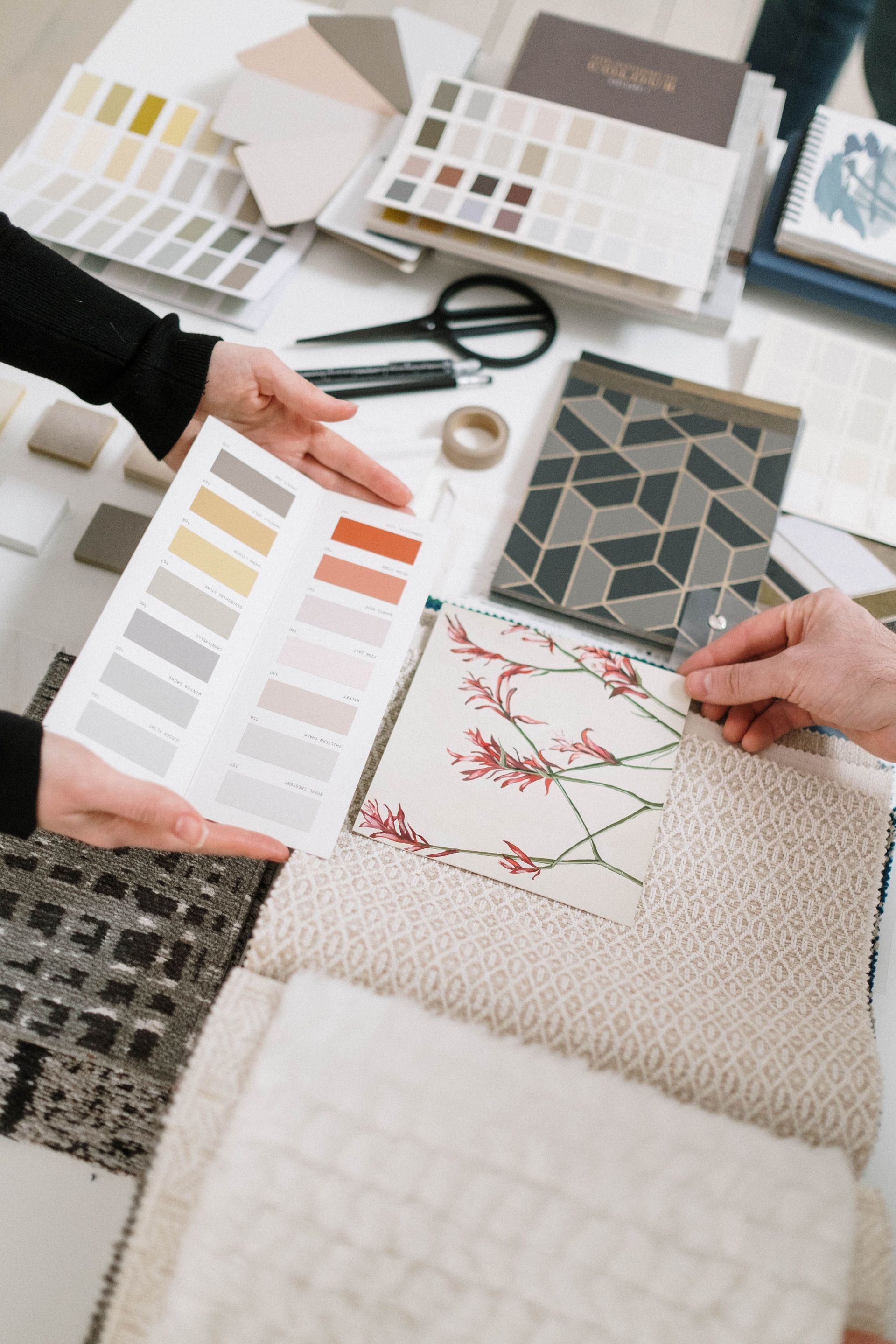 Des mains comparent des échantillons de tissu et de papier peint sur une table avec des nuanciers.