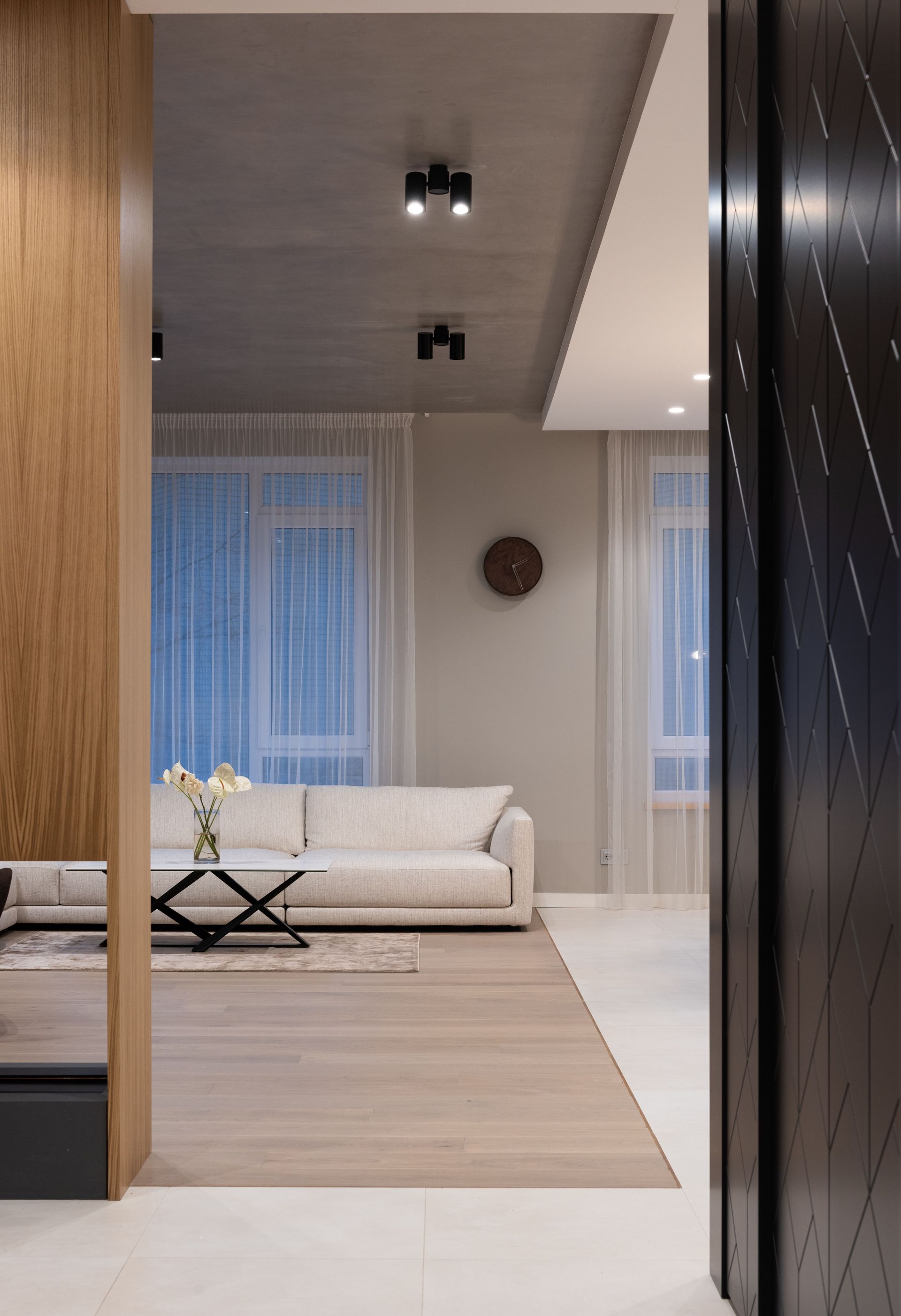 Salon moderne avec canapé beige, parquet et grandes fenêtres, vu à travers une porte