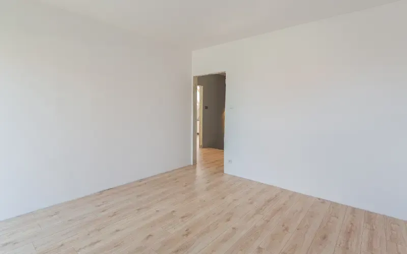 Pièce blanche vide avec parquet clair et porte ouverte.