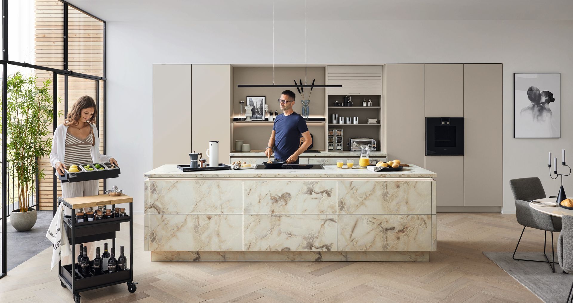 Hochwertige Küche im Marmor-Look mit großer Kücheninsel, ein Mann kocht an dem Herd mit eingelassenem Downdraft