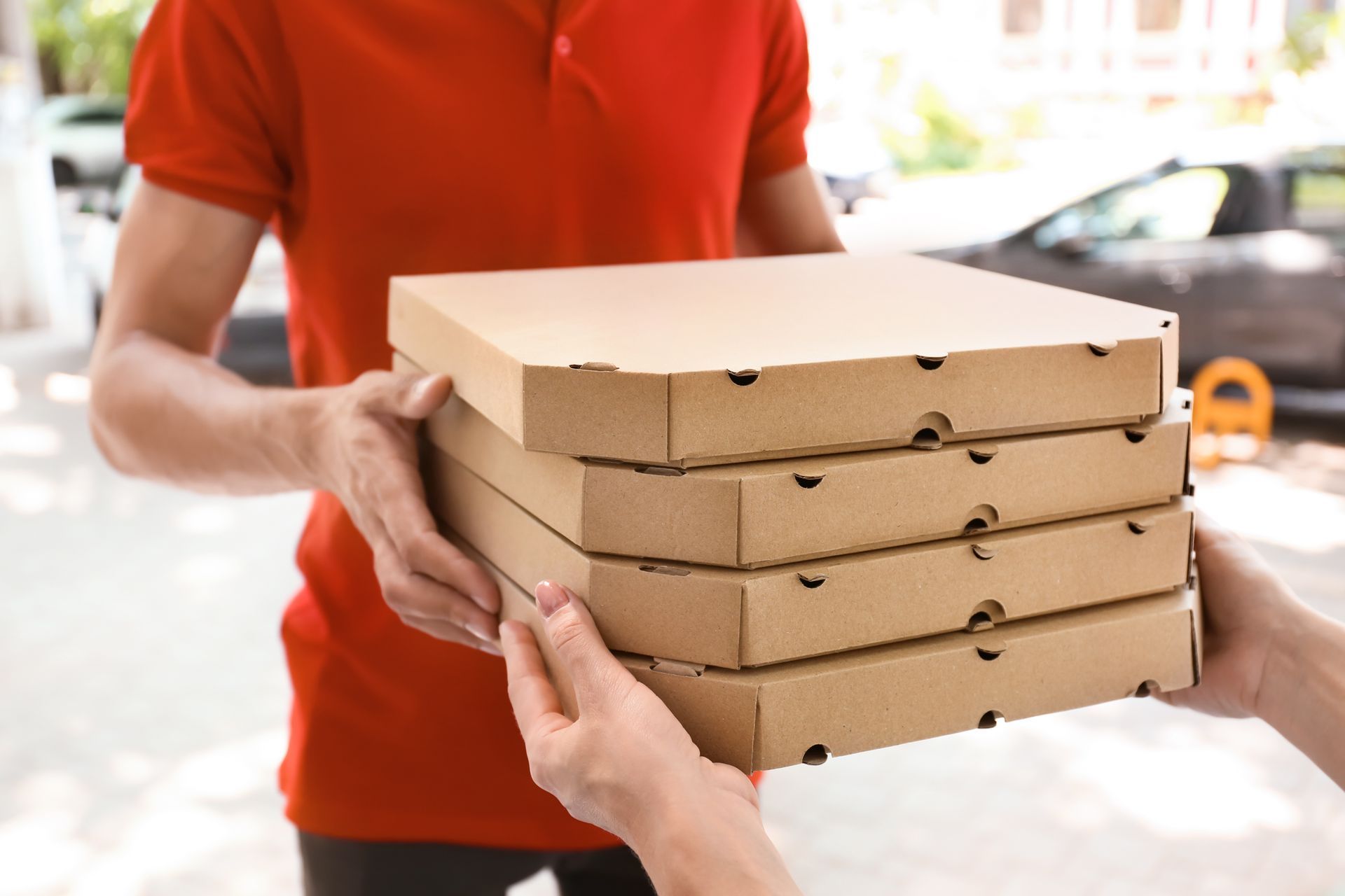 Une personne en chemise rouge tend une pile de boîtes à pizza à une autre personne