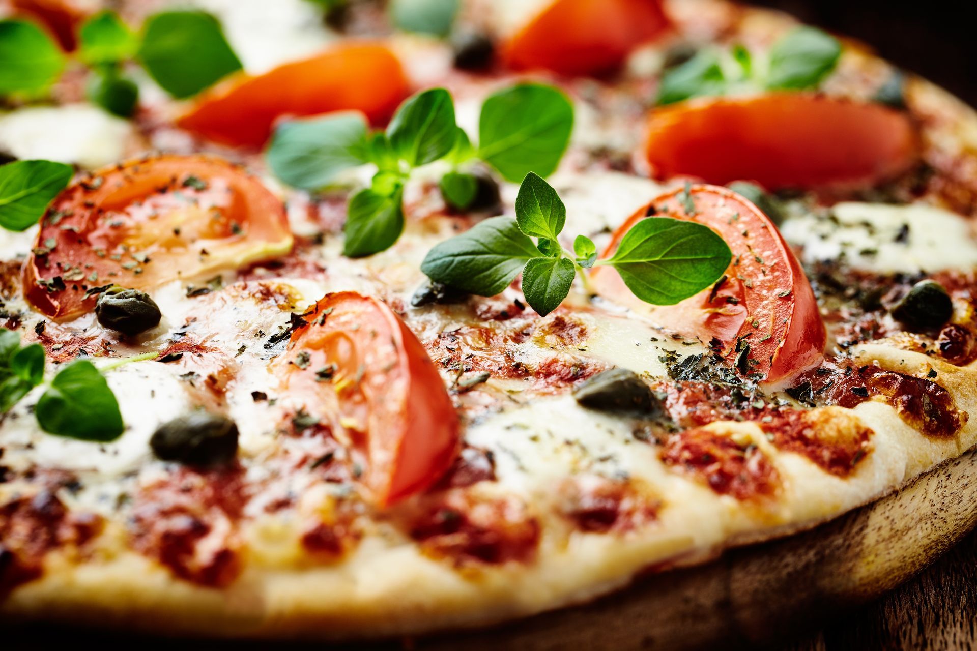 Gros plan d'une pizza au fromage garnie de tomates, de basilic et d'herbes aromatiques, posée sur une planche en bois