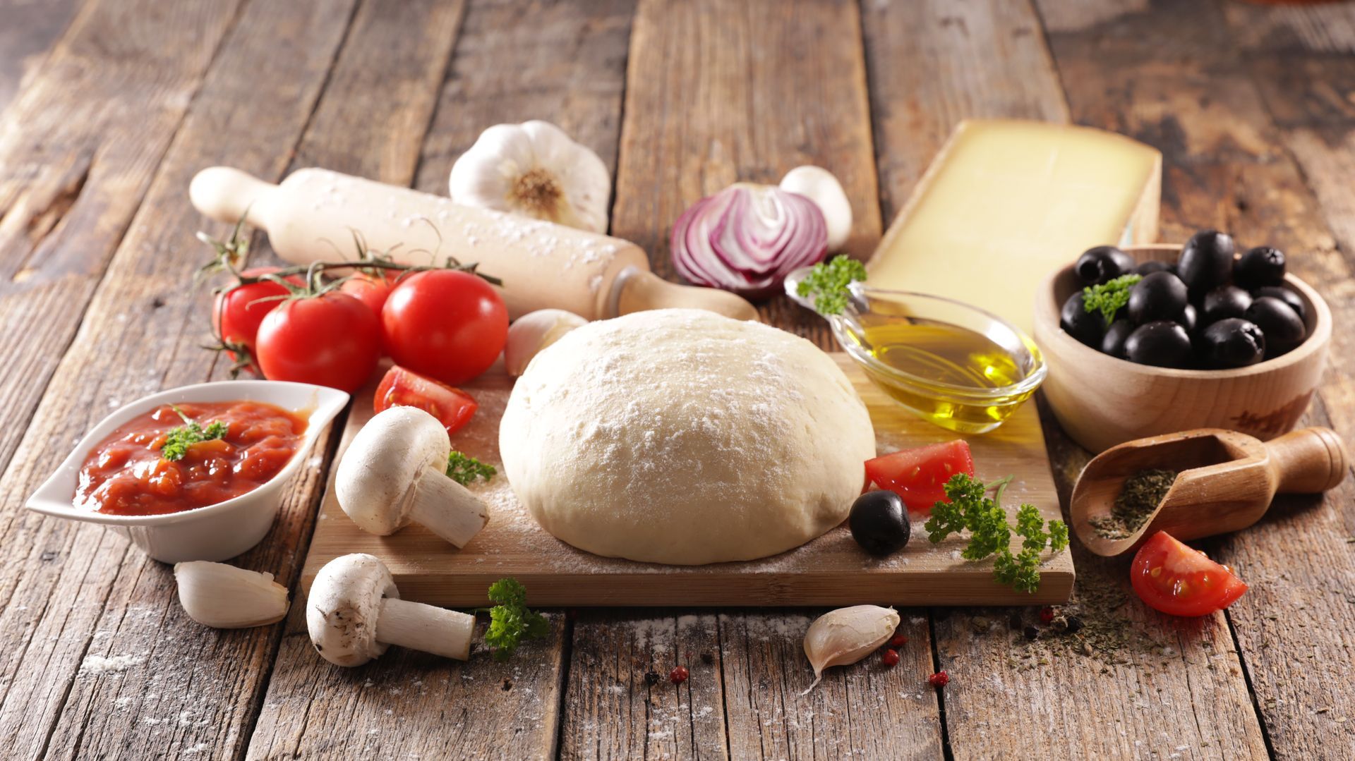 Ingrédients frais pour pizza sur une table rustique : pâte, tomates, olives, fromage, champignons, huile et basilic