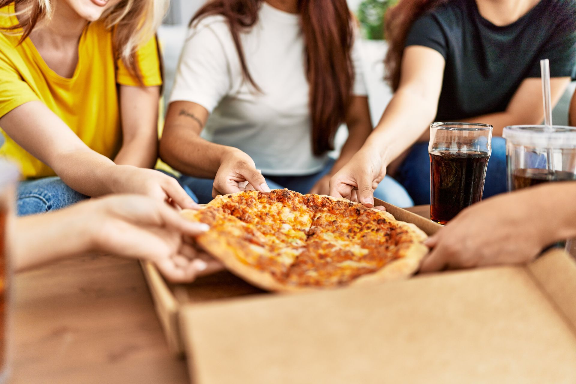 Des personnes partagent des parts de pizza au fromage à une table, avec des boissons à côté