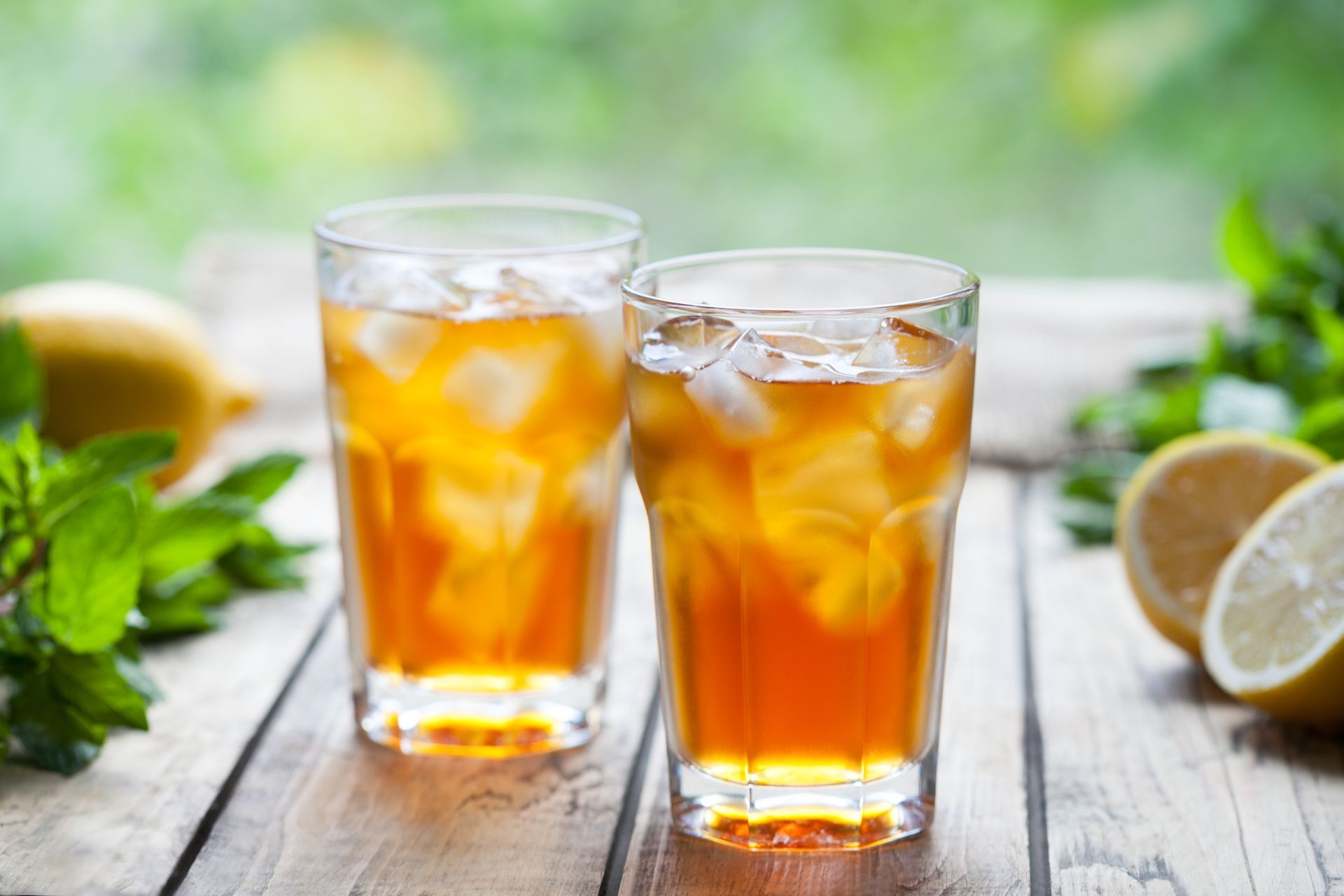 Deux thés glacés dans des verres, posés sur une table en bois avec des citrons et de la menthe, à l'extérieur