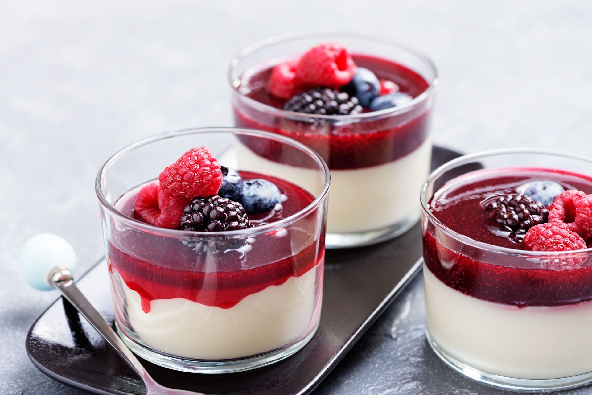 Trois verrines en verre garnies de crème et de coulis de fruits rouges, surmontées de framboises et de myrtilles