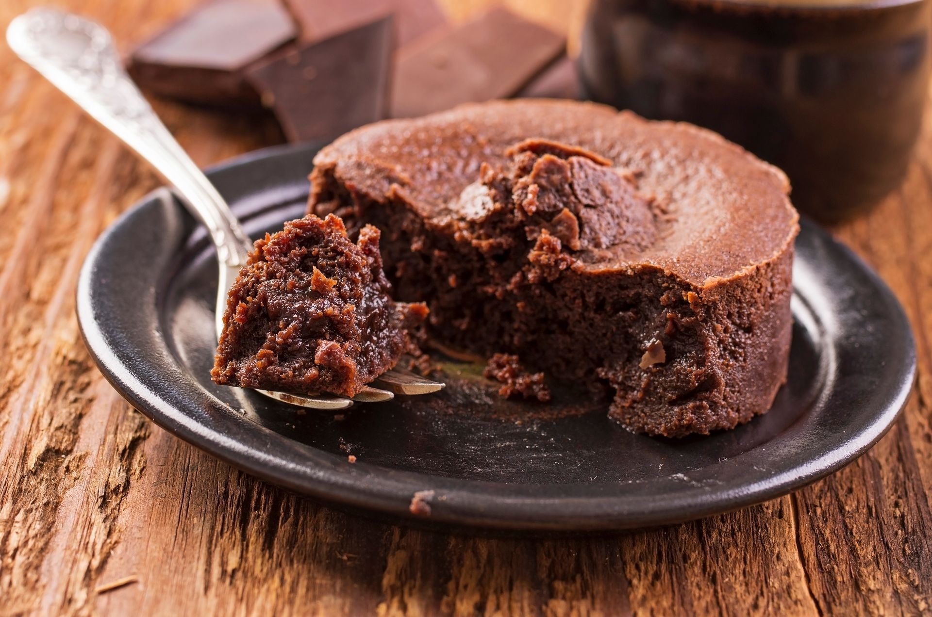 Gâteau au chocolat à cœur fondant présenté sur une assiette avec une cuillère, laissant apparaître un centre coulant, sur une table rustique en bois