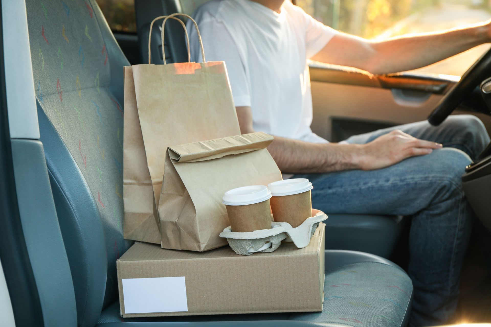 Des sacs de plats à emporter et un café sur un siège auto à côté du conducteur dans un véhicule