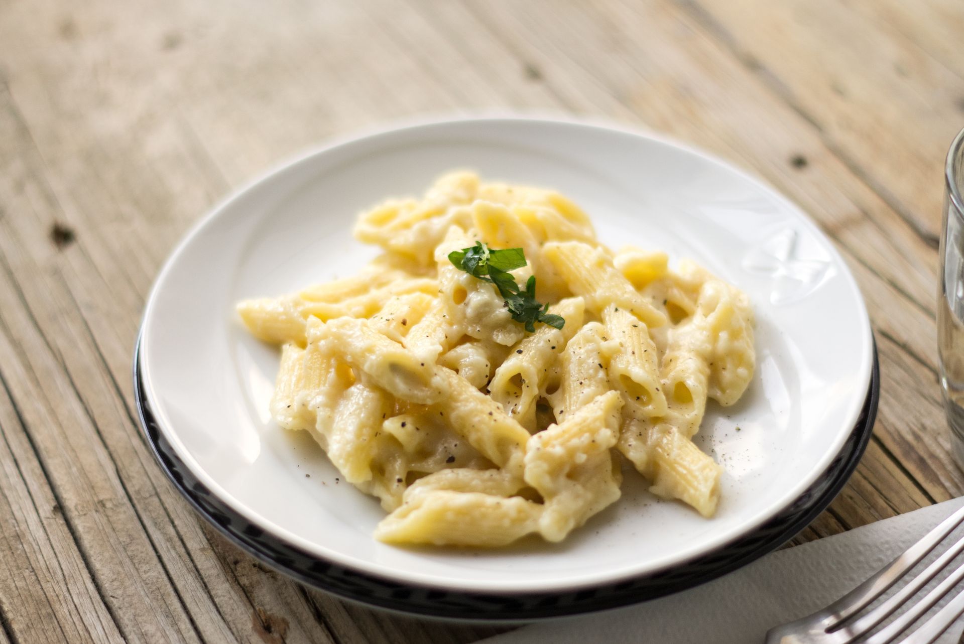 Assiette de pâtes crémeuses sur un plat blanc, garnie de persil, sur une table rustique en bois