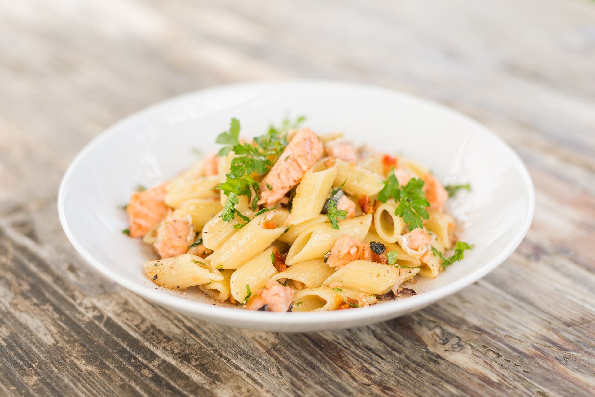 Pâtes au saumon et au persil dans un bol blanc sur une table rustique en bois