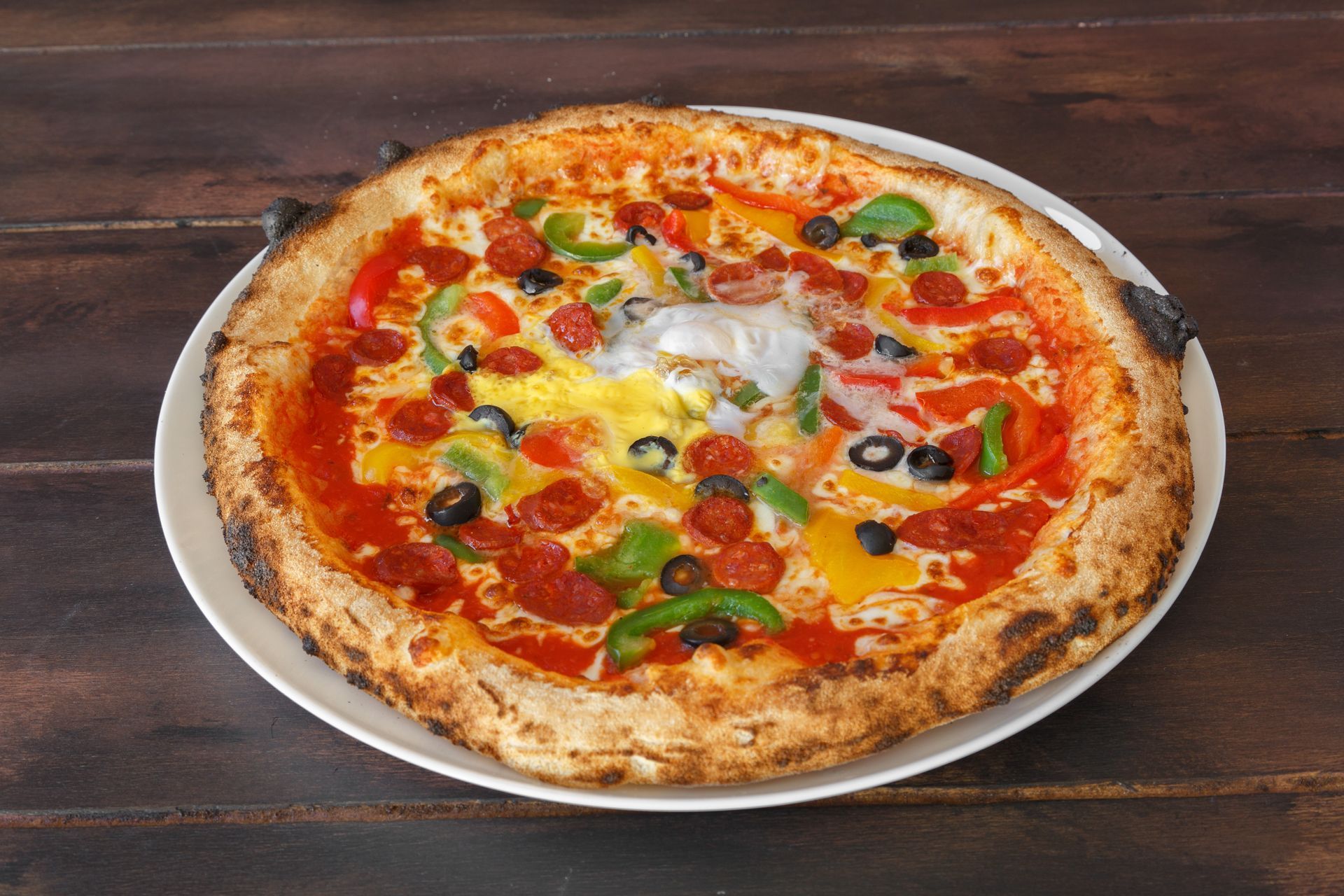 Pizza garnie d'olives, de basilic et de fromage fondu sur une assiette blanche posée sur une table en bois