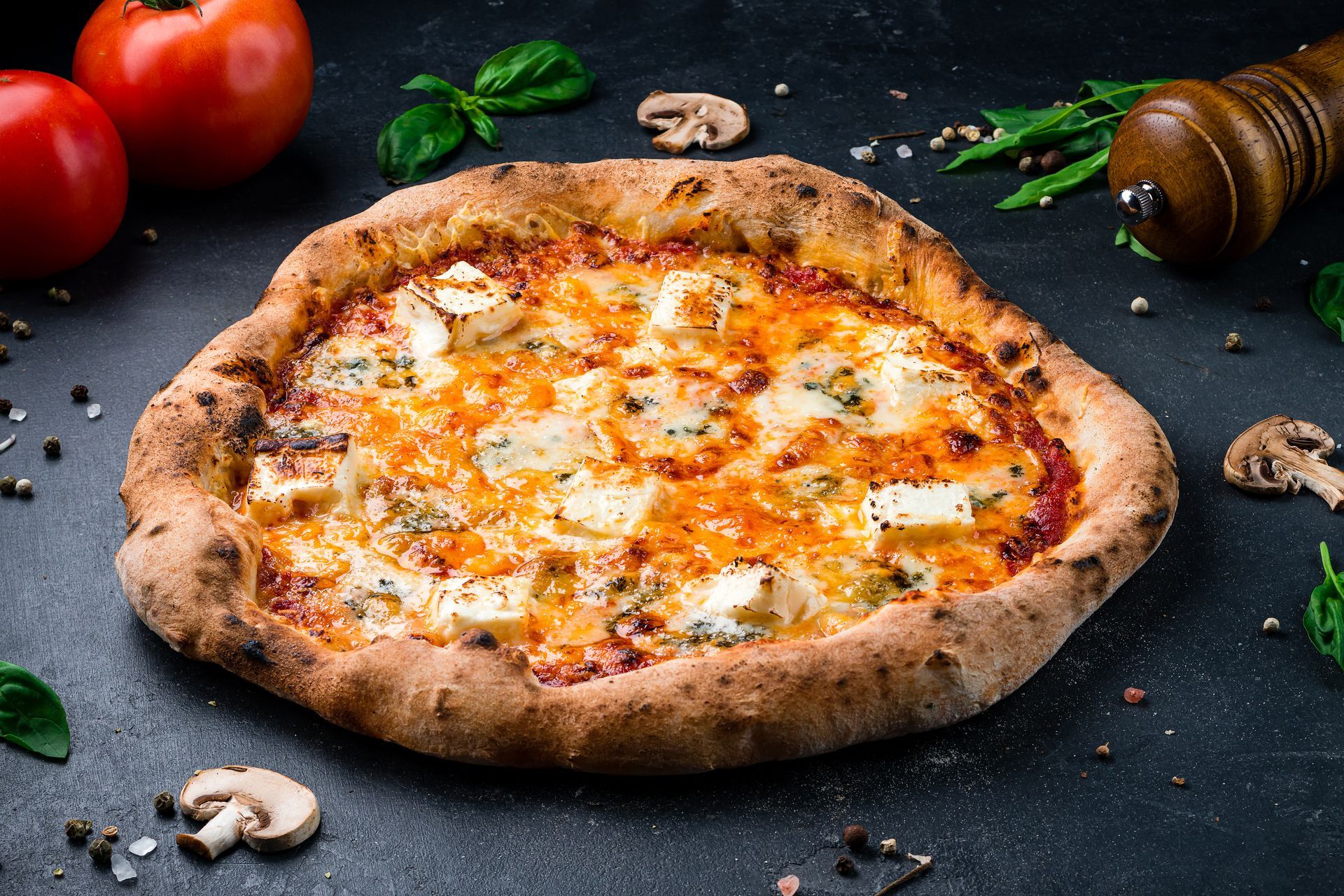 Pizza au fromage cuite au feu de bois sur une table sombre, avec tomates, basilic, champignons et un rouleau à pâtisserie