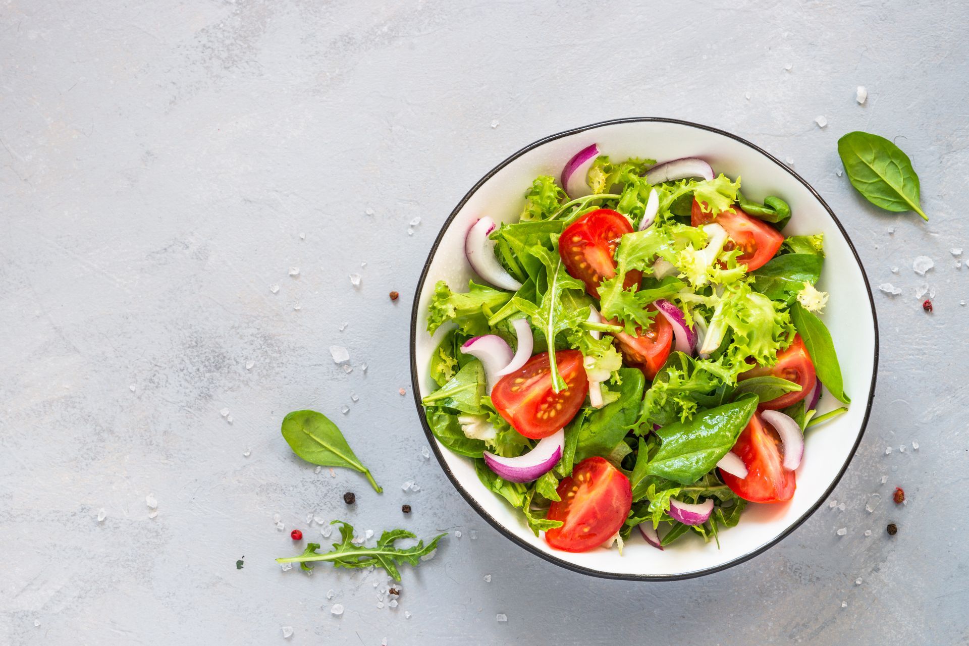 Salade verte fraîche avec tomates, oignon et herbes dans un bol blanc sur une surface gris clair