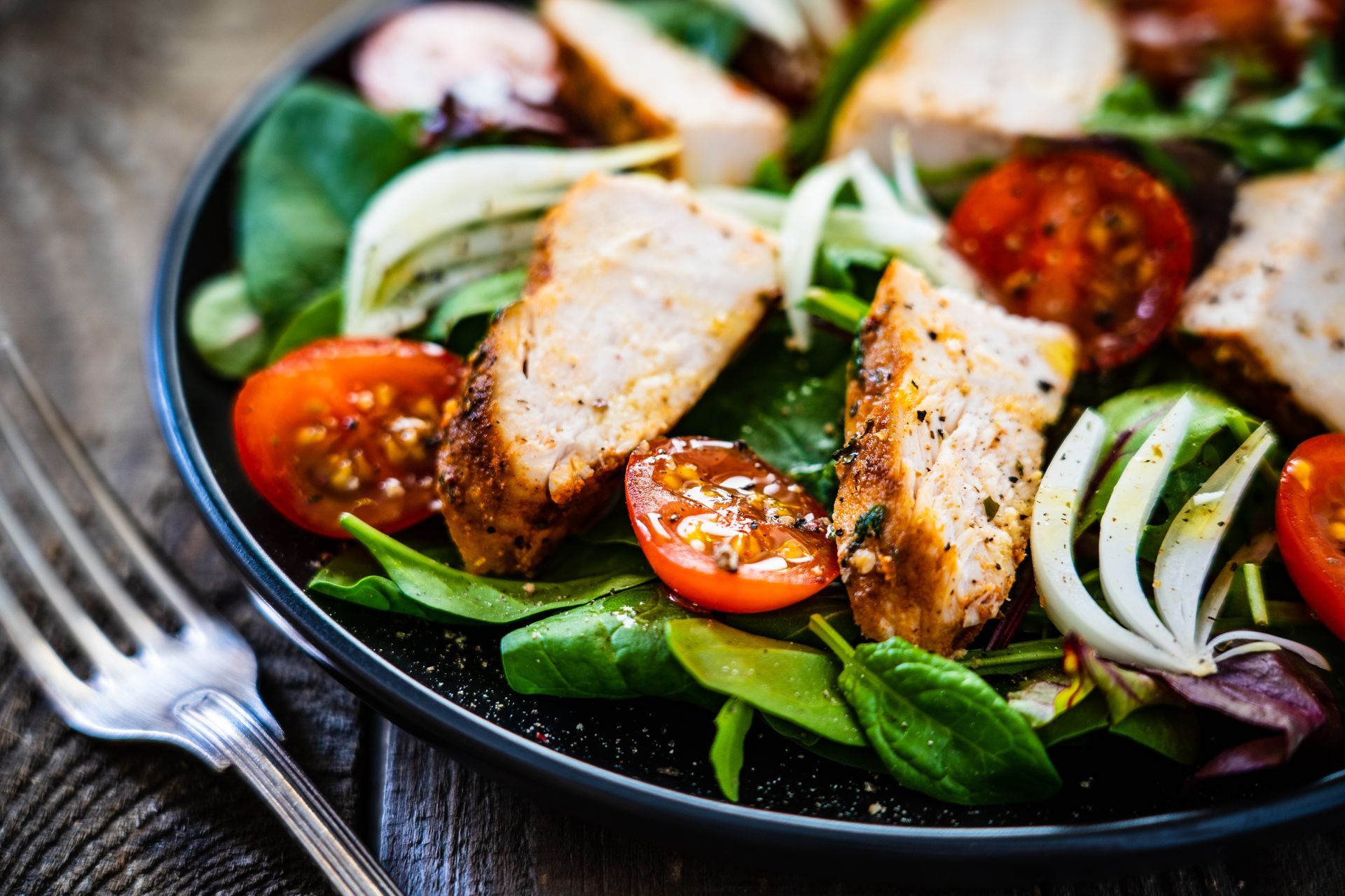 Salade de poulet grillé aux épinards, tomates cerises, oignons et vinaigrette, servie dans un bol noir