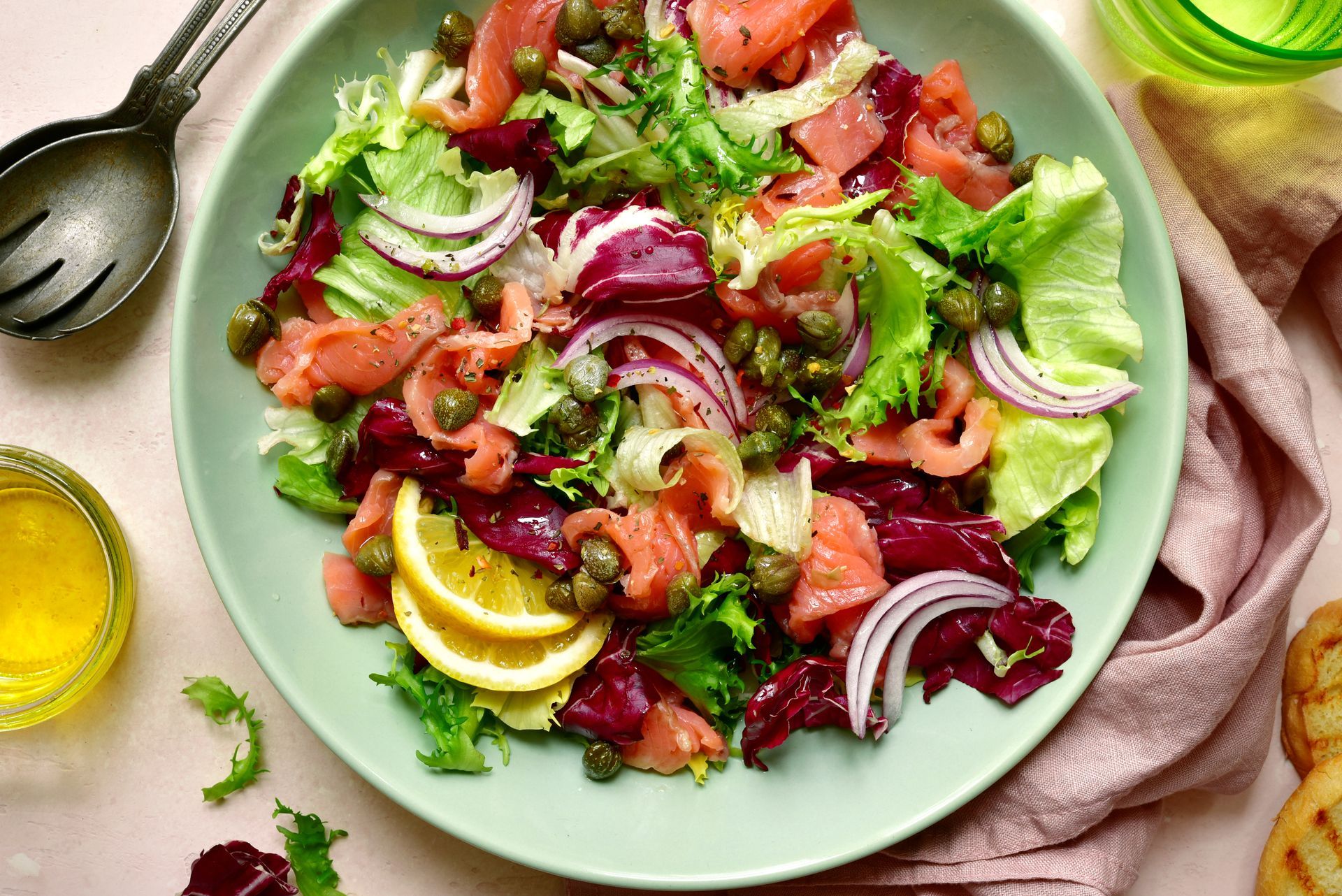 Salade composée de saumon, oignon rouge, quartiers de citron et fines herbes, servie sur une assiette verte avec une vinaigrette