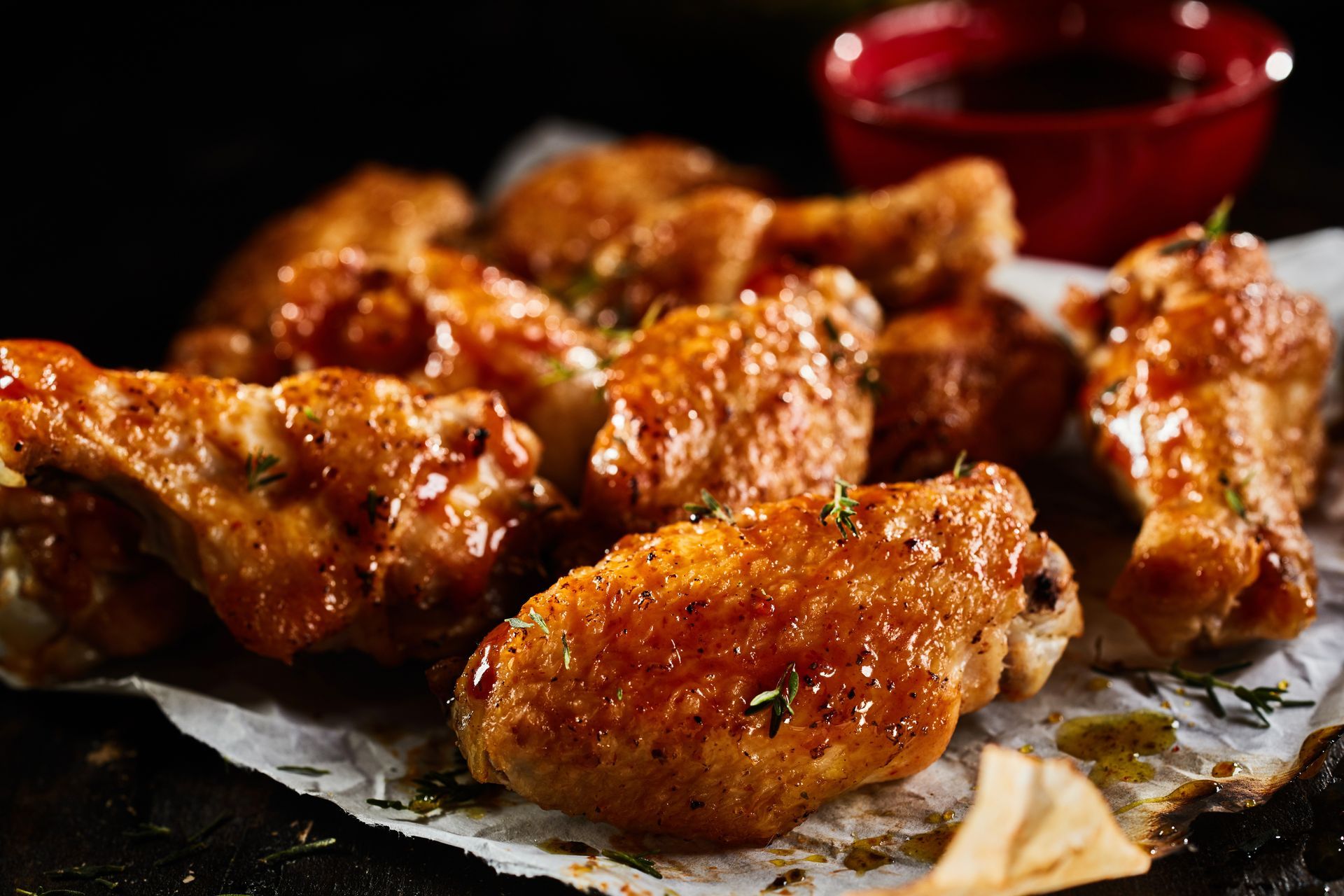 Ailes de poulet sur du papier sulfurisé avec un petit bol de sauce