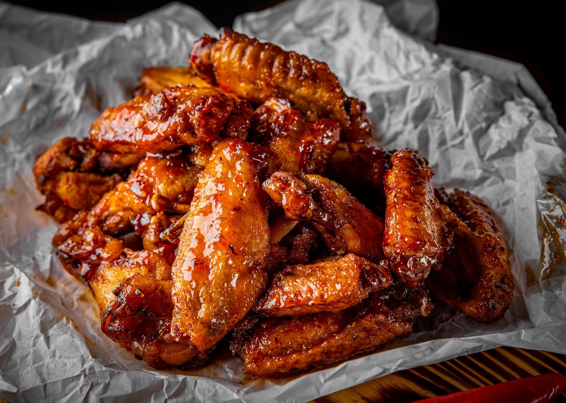 Un tas d'ailes de poulet dorées et nappées de sauce, disposées sur du papier sulfurisé froissé