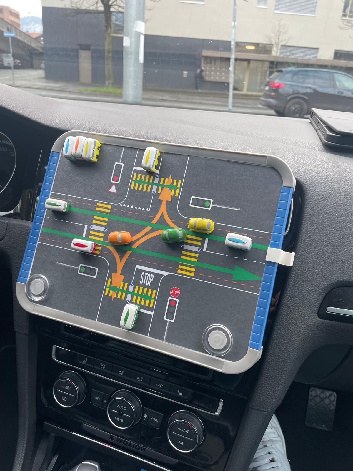 Ein Fahrschüler übt Fahrmanöver; der Fahrlehrer zeigt im Auto auf eine Skizze auf einem Klemmbrett.