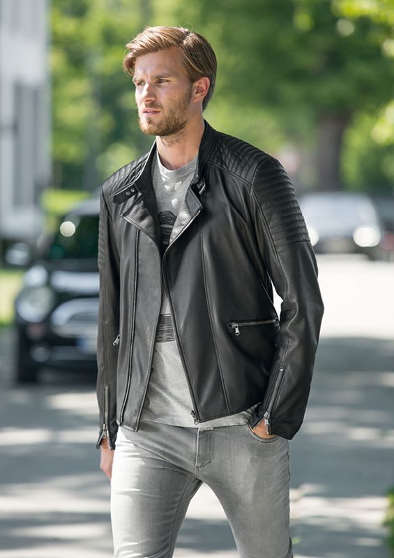 Ein Mann in einer schwarzen Lederjacke und grauen Jeans geht eine Straße entlang.