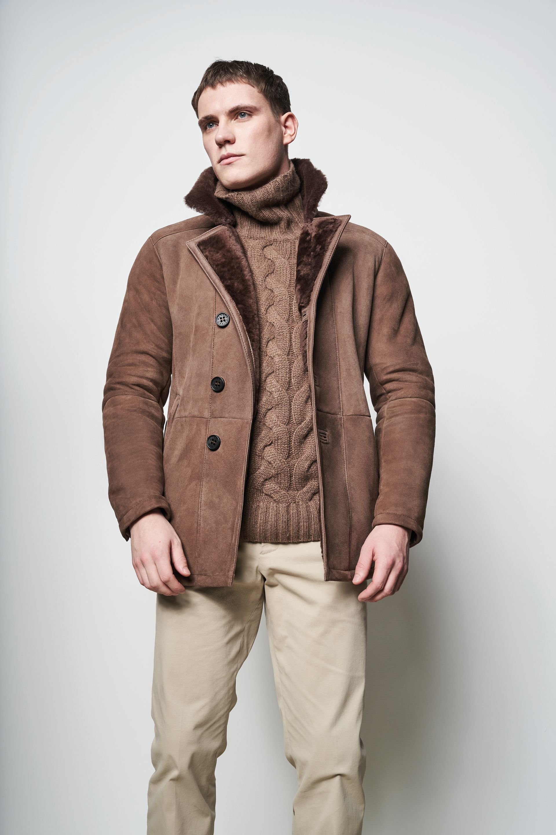 Ein Mann trägt einen braunen Mantel und einen Rollkragenpullover.