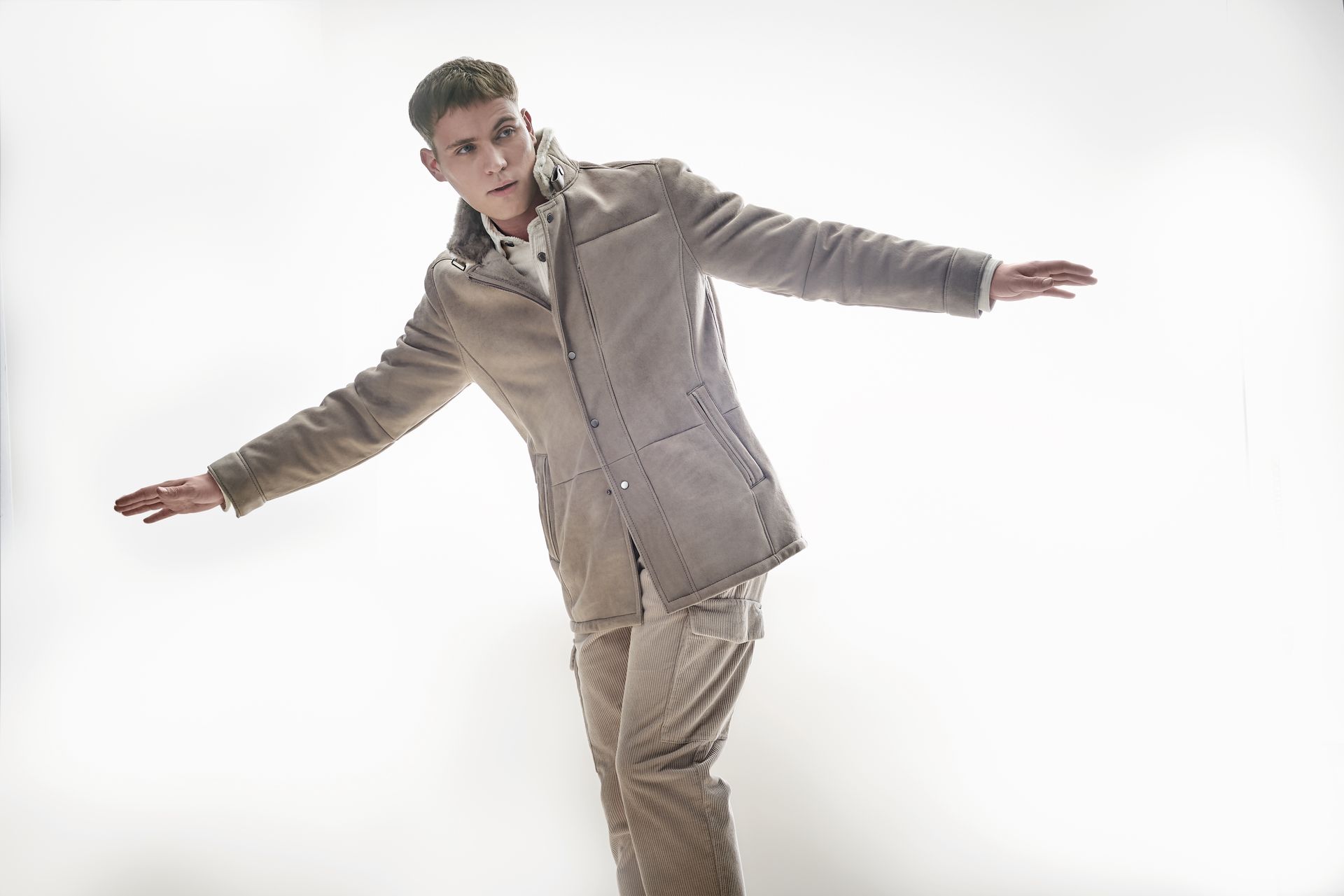 Ein Mann in Jacke und Hose steht mit ausgestreckten Armen da.