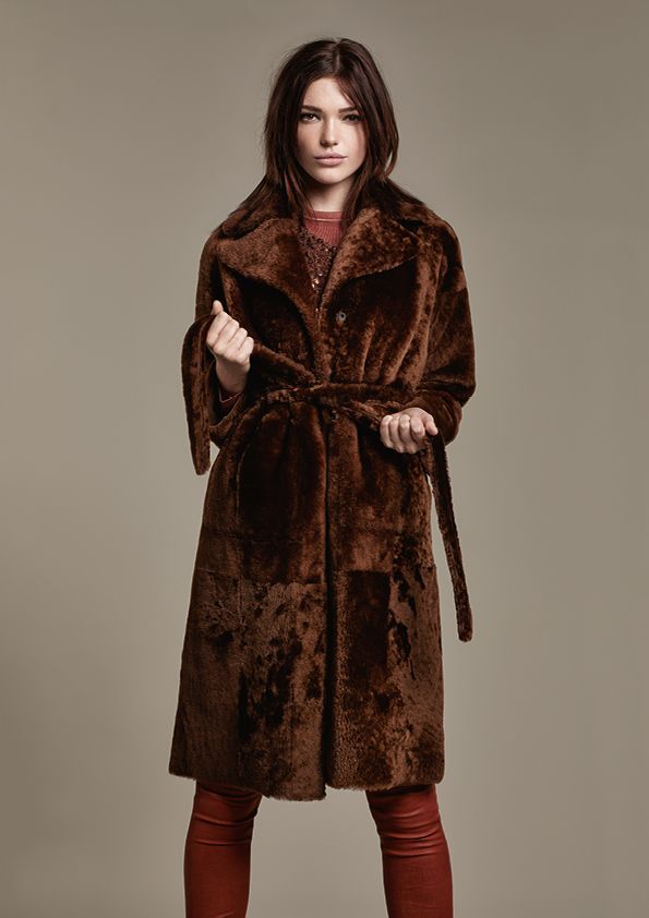 Eine Frau trägt einen braunen Pelzmantel und eine rote Hose.