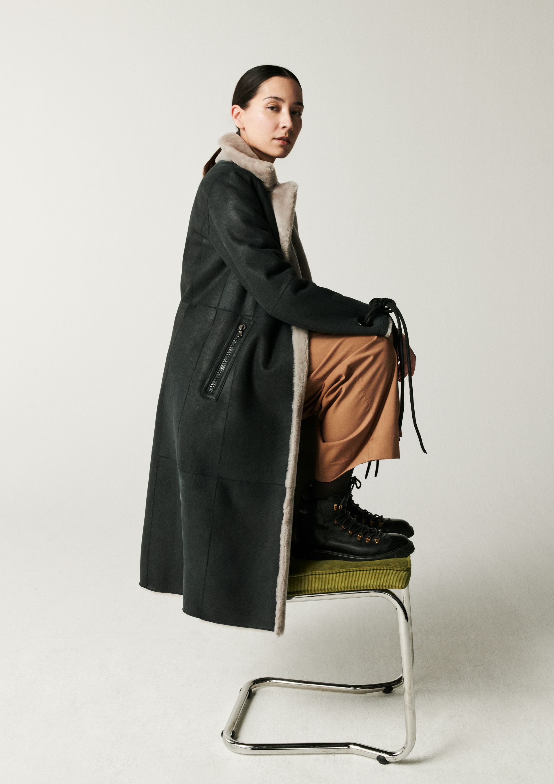 Eine Frau in einem schwarzen Mantel sitzt auf einem Stuhl.