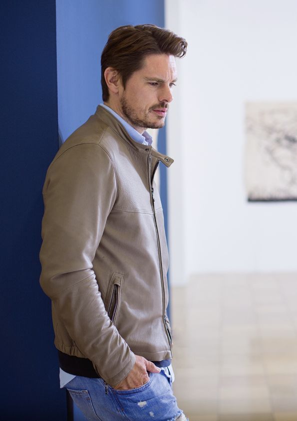 Ein Mann in einer Lederjacke lehnt an einer Wand.